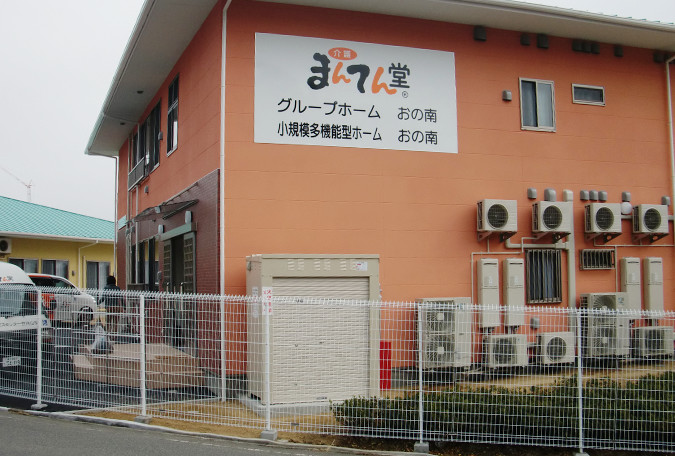 オレンジ色の外壁が特徴的な介護施設の建物外観。施設名看板が見える。